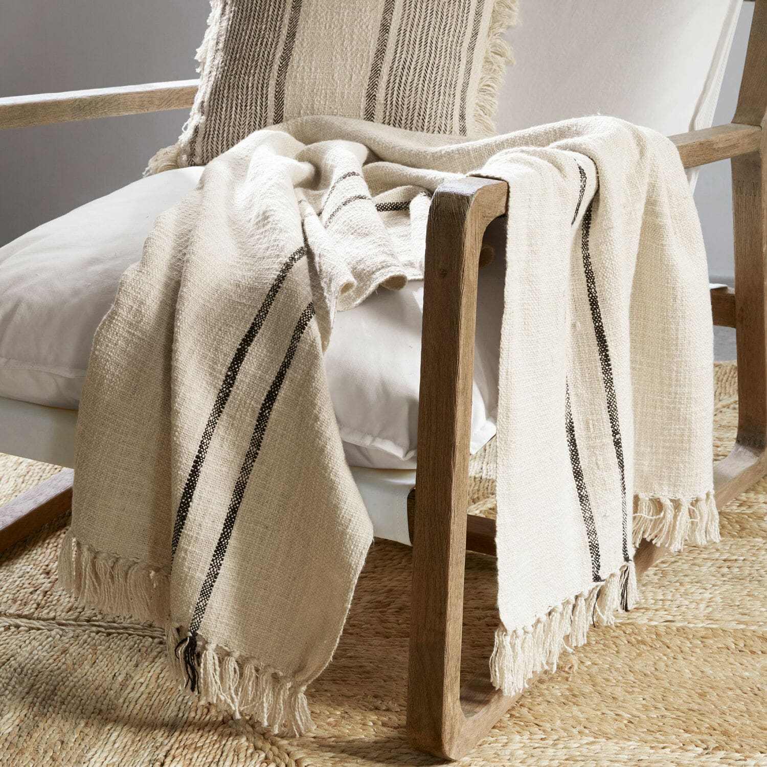 Plaid Toos Plaid beige en coton avec rayures noires et franges sur fauteuil en bois dans un salon