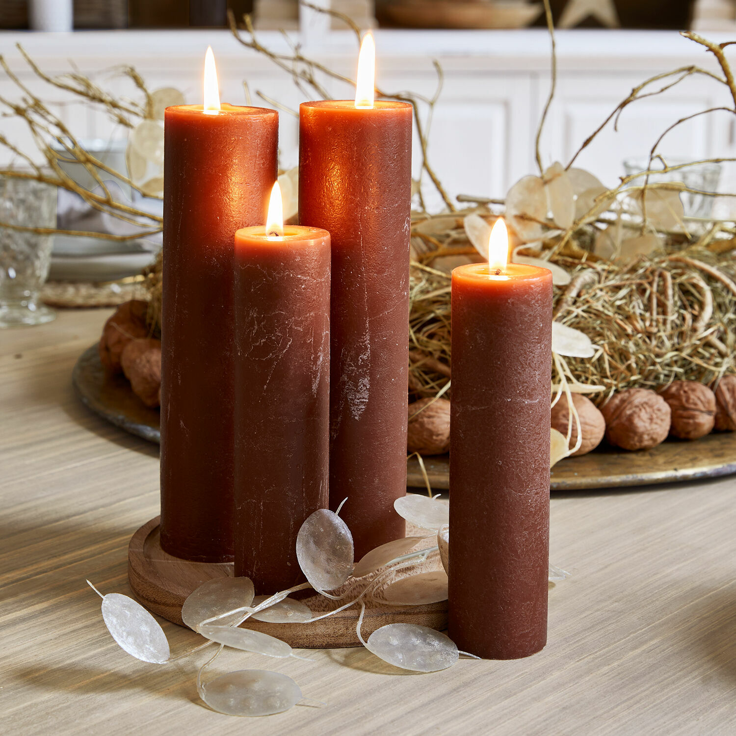 Lot de 4 bougies Avinal Quatre bougies en cire marron allumées sur un support en bois avec décoration sur la table