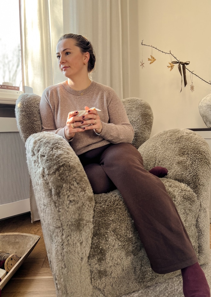 Fauteuil moelleux en fausse fourrure grise dans un intérieur cosy avec femme tenant une tasse