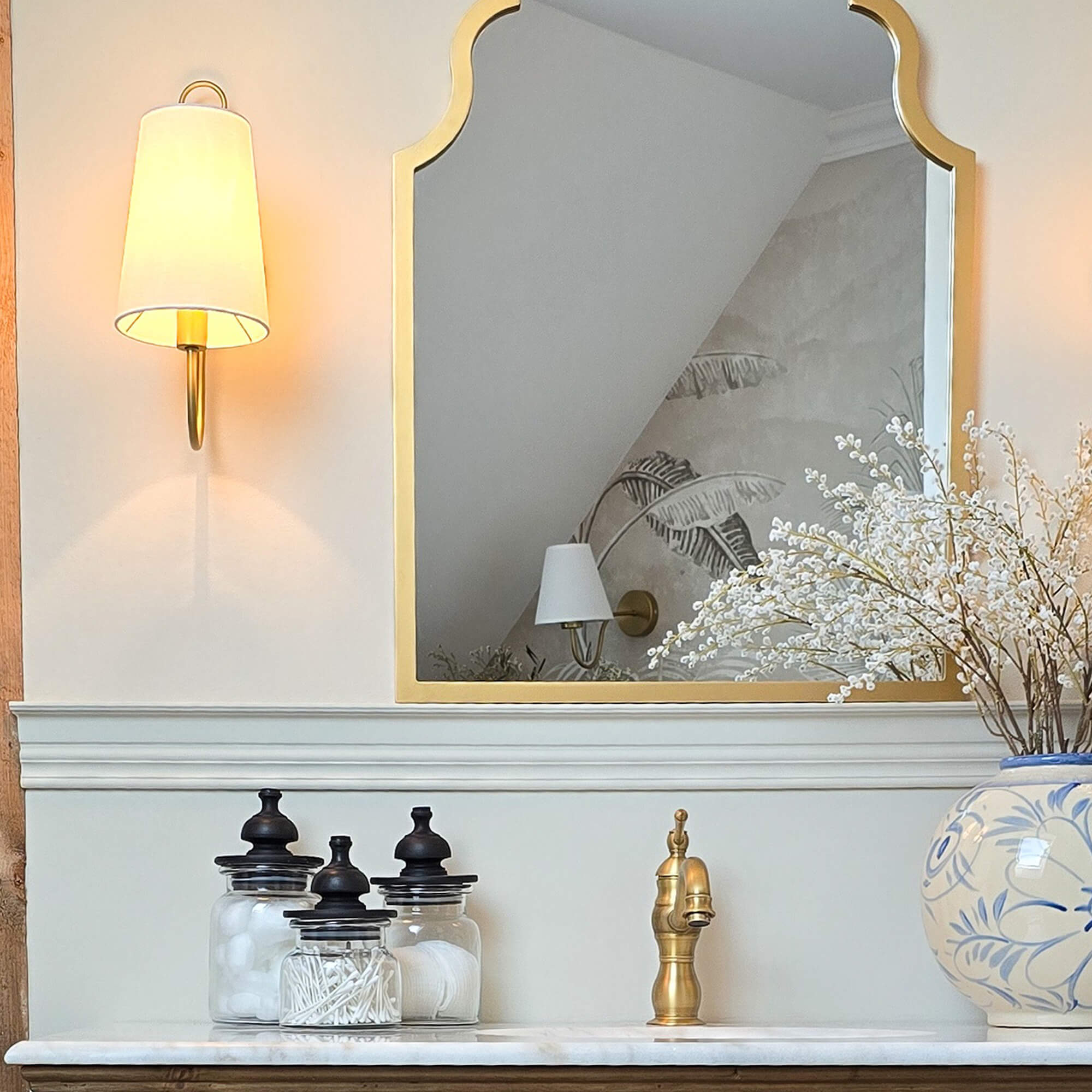 Miroir doré à cadre décoratif au-dessus d'un lavabo en marbre avec robinet en laiton et bocaux en verre