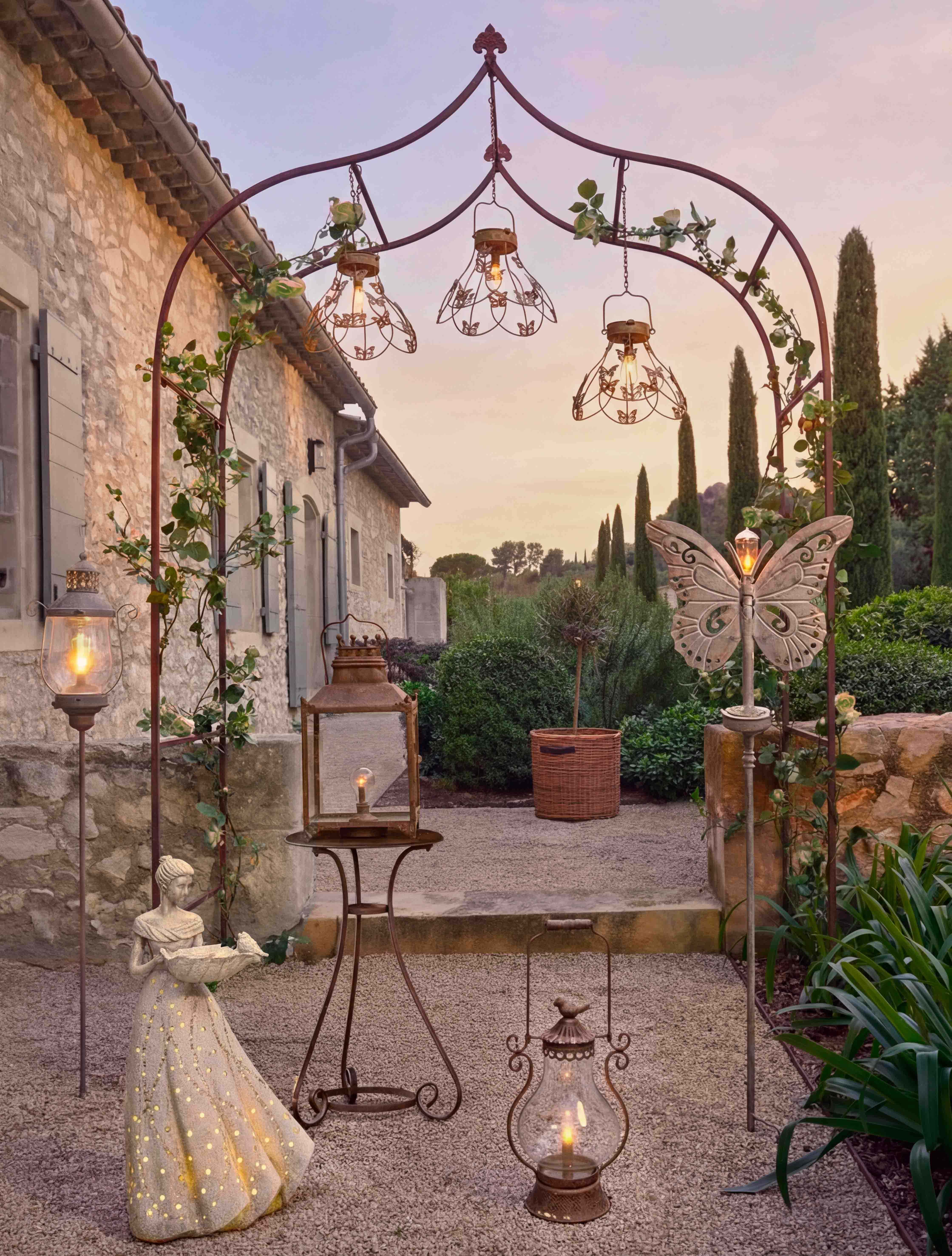Arche en métal décorative avec lanternes et statue de femme éclairée dans un jardin au crépuscule