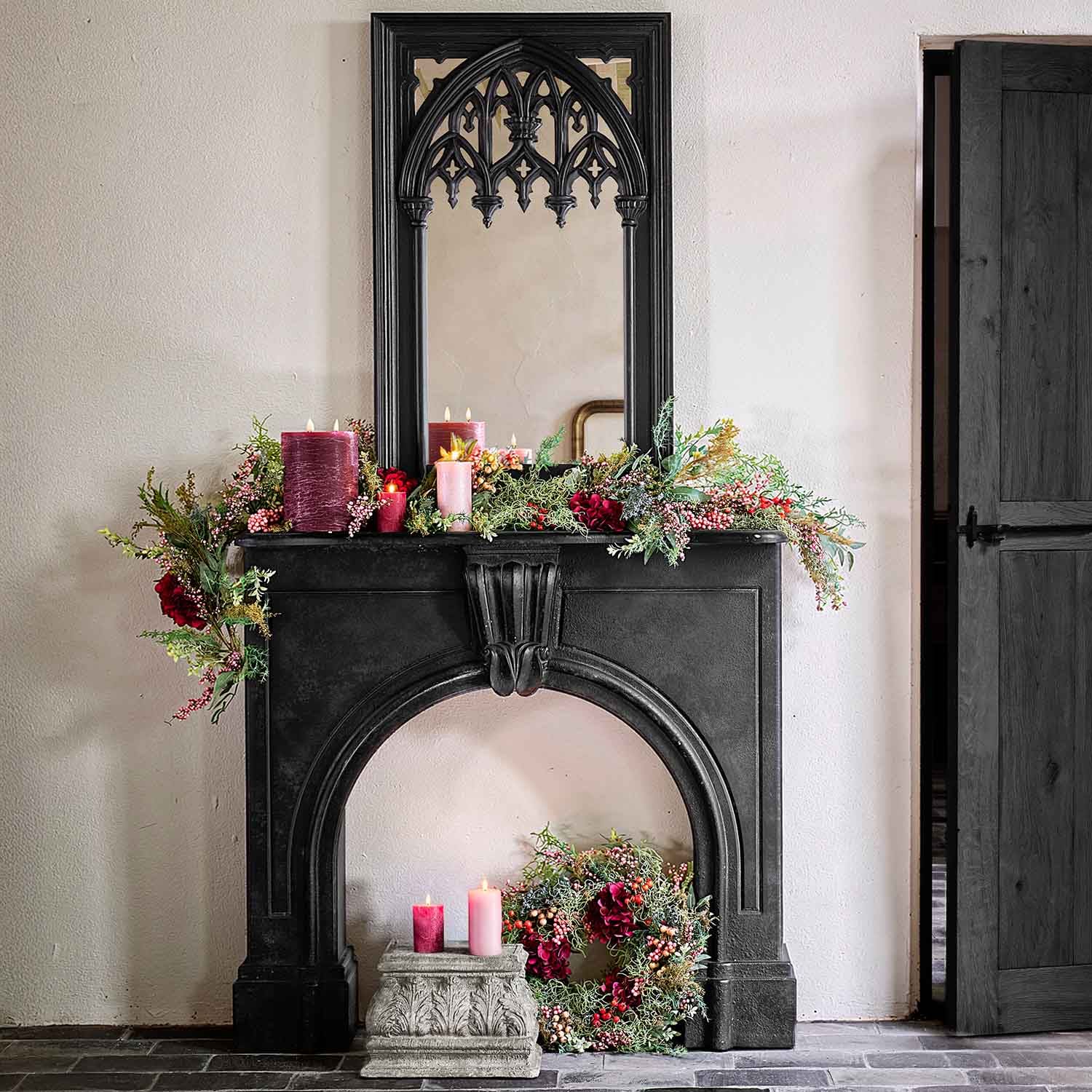 Cheminée noire décorative avec miroir gothique, ornée de bougies rouges et guirlandes vertes pour décoration intérieure