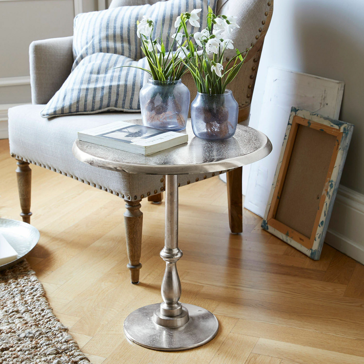 Table d'appoint Eppeville Table d'appoint ronde en métal argenté avec vases décoratifs et livre dans un salon lumineux