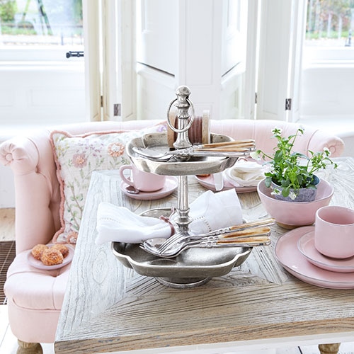 Présentoir à deux niveaux en métal sur table avec vaisselle rose et plante verte dans un intérieur lumineux