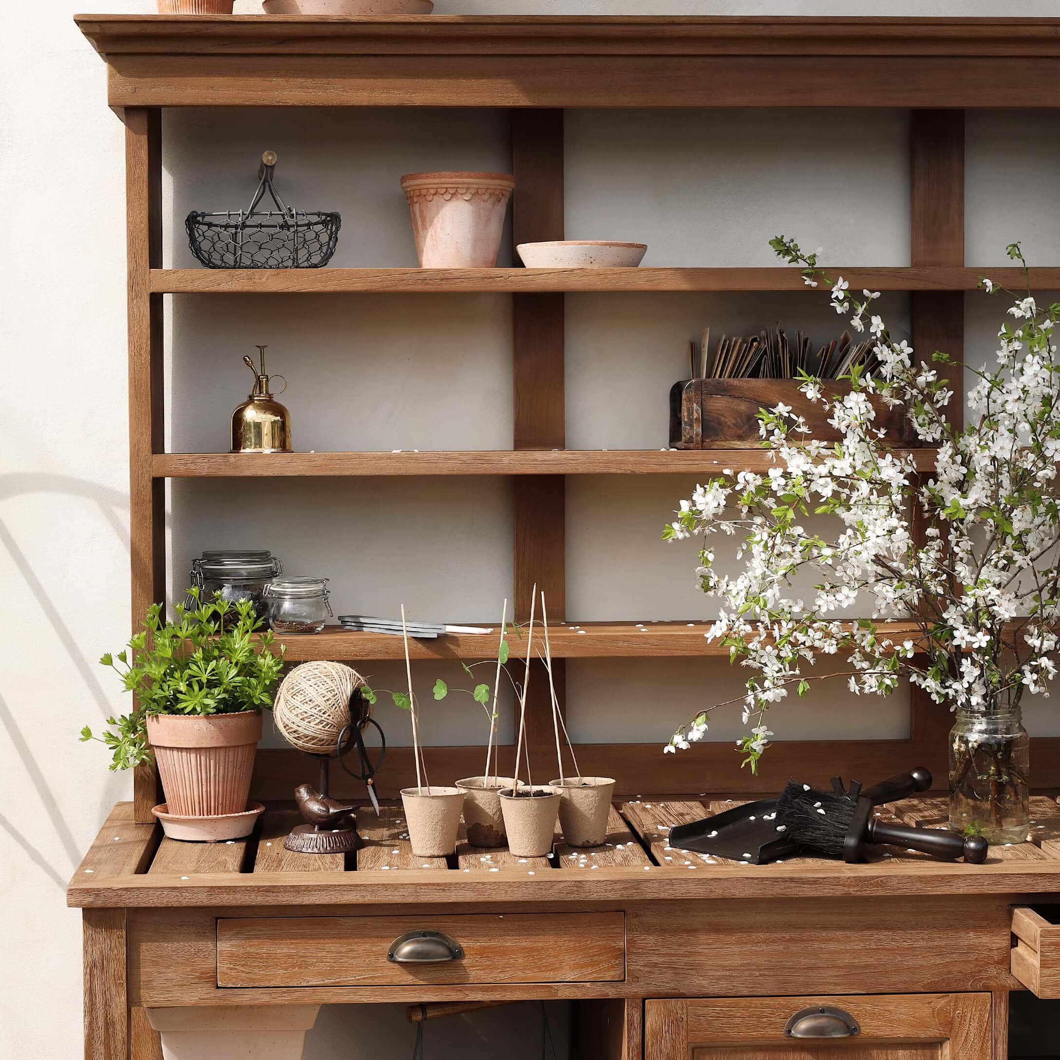 Table de jardin en bois avec pots, outils de jardinage et branches fleuries dans un bocal en verre