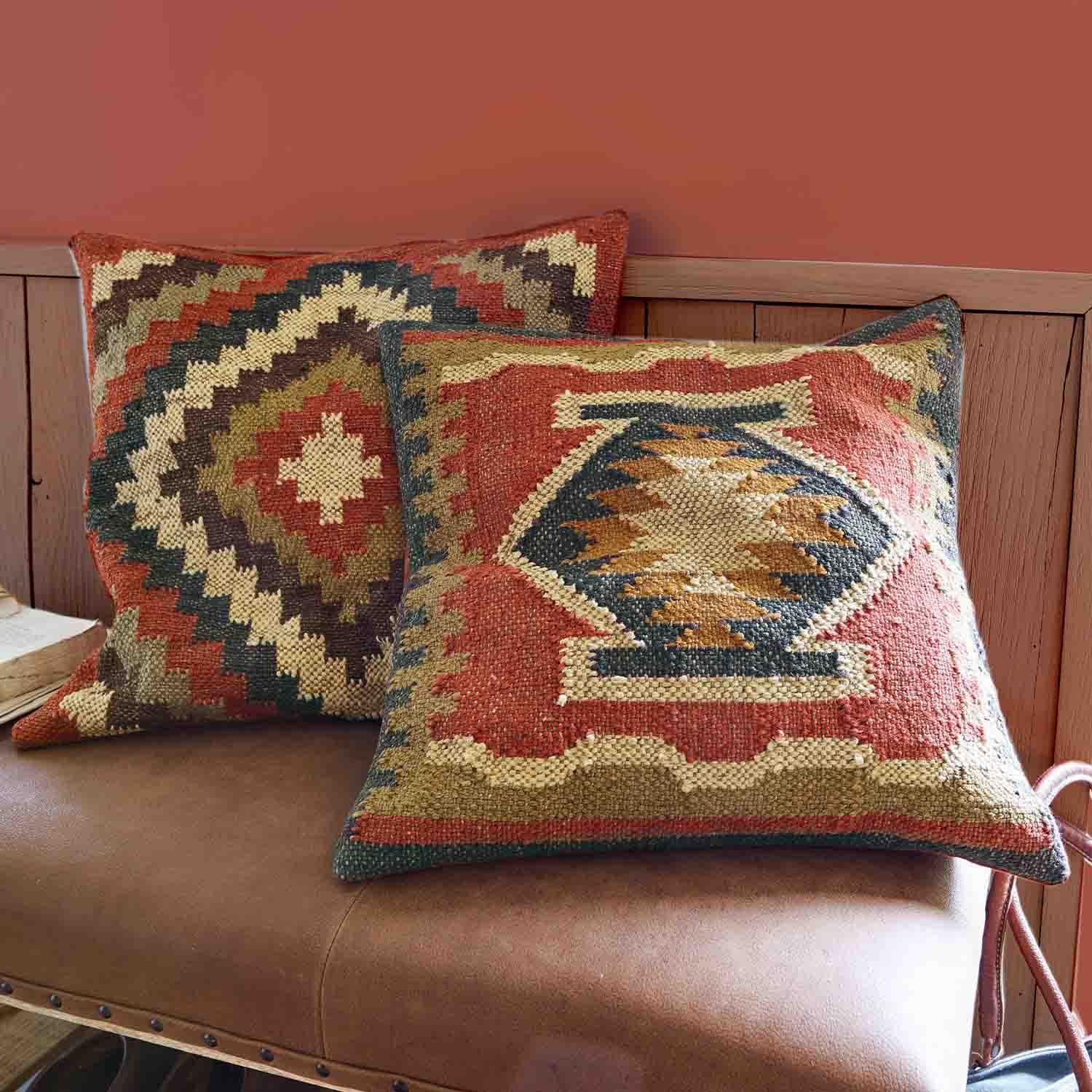 Deux coussins décoratifs en tissu avec motifs géométriques dans des tons chauds rouge et beige sur un canapé en cuir