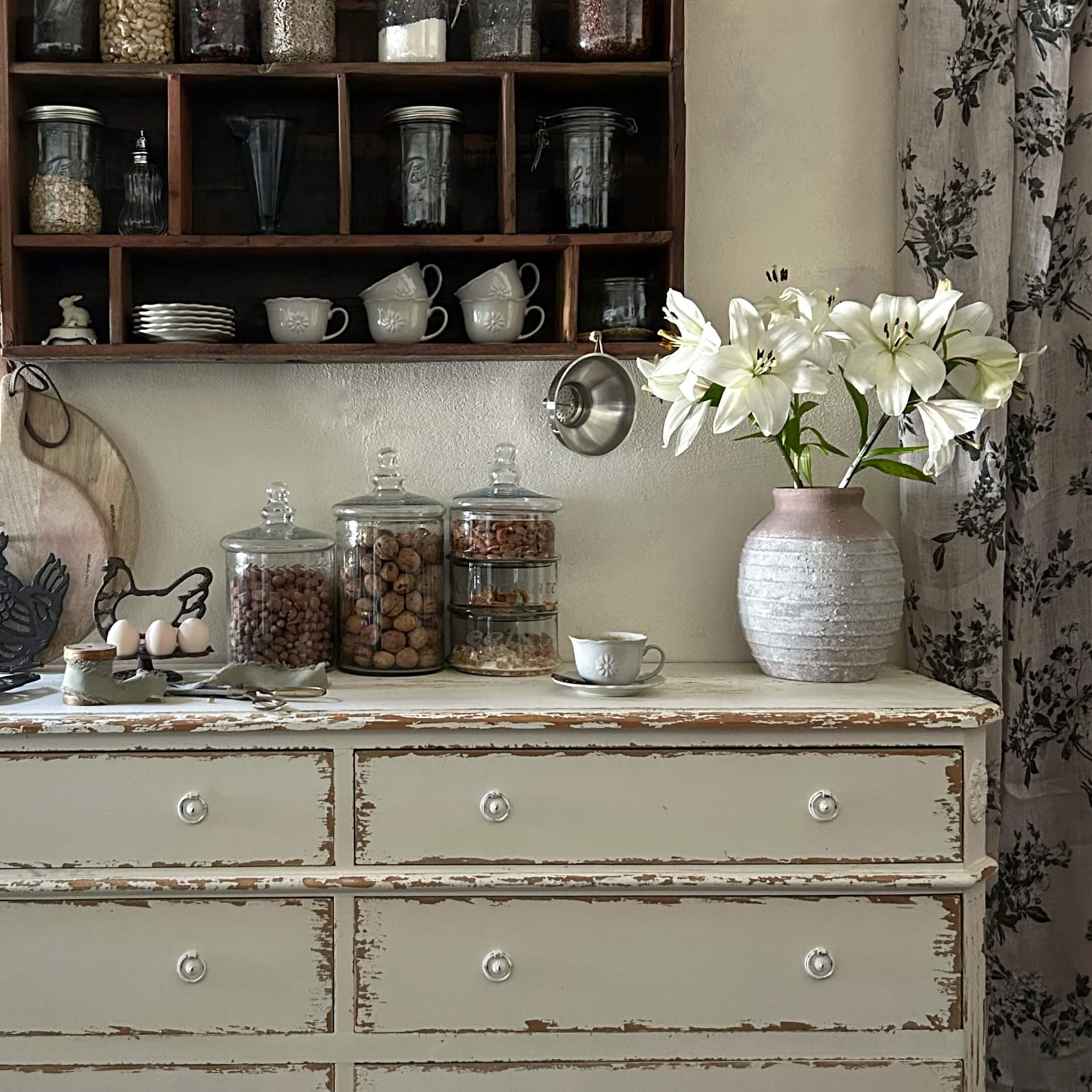 Commode blanche rustique avec vase en céramique rose et lys blancs dans une cuisine vintage