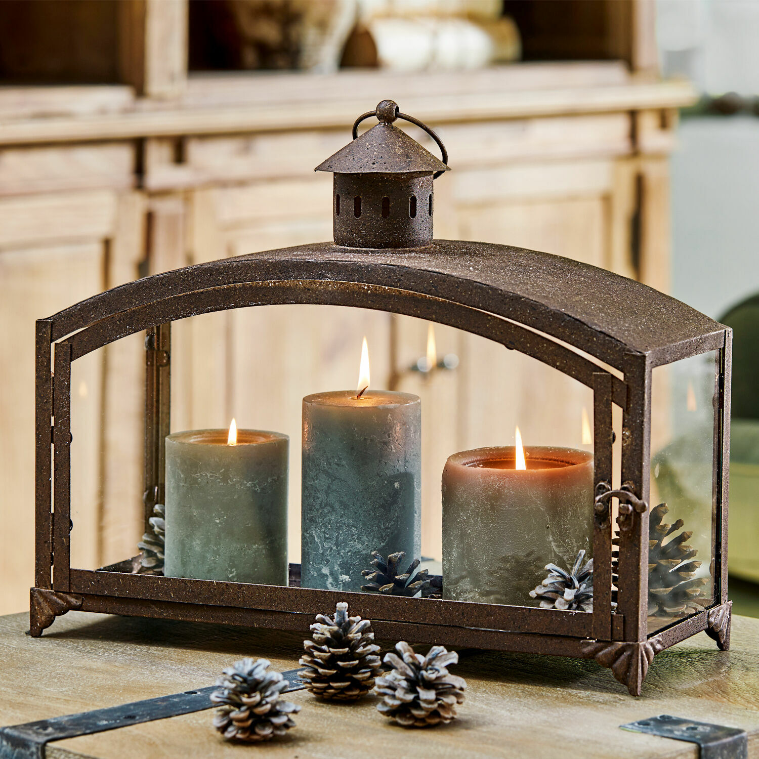 Lanterne en métal avec trois bougies vertes et pommes de pin sur une table en bois, décoration intérieure