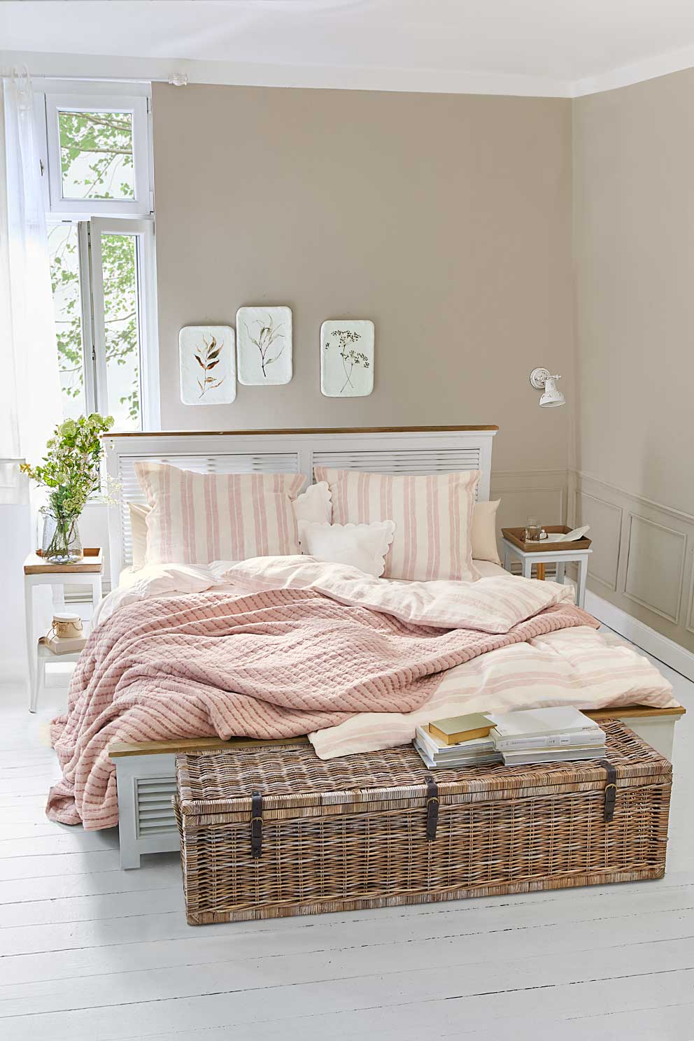Parure de lit rayée rose et blanche sur lit avec coffre en osier, chambre lumineuse et décorée