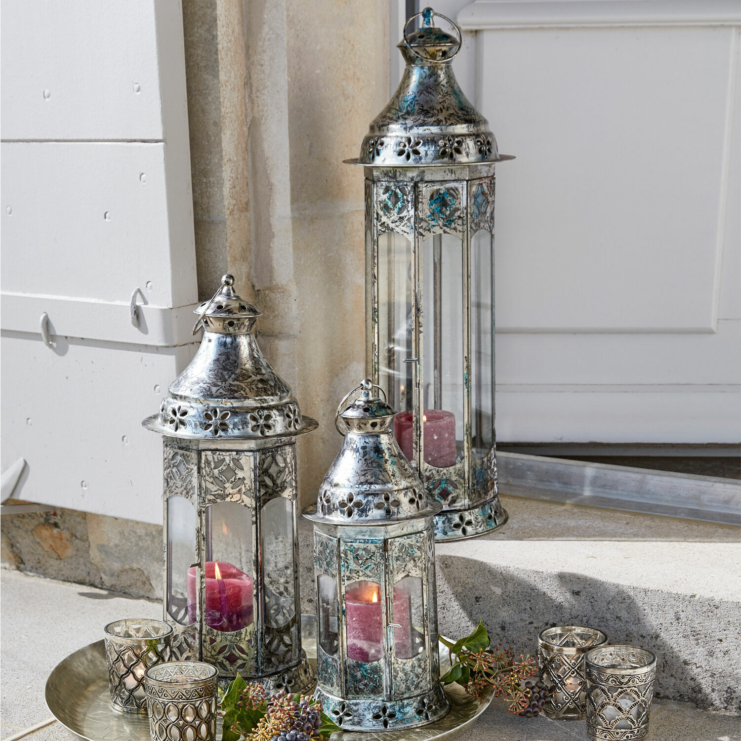 Lot de 3 lanternes Aylin Ensemble de trois lanternes en métal argenté avec bougies rouges et décorations sur un plateau