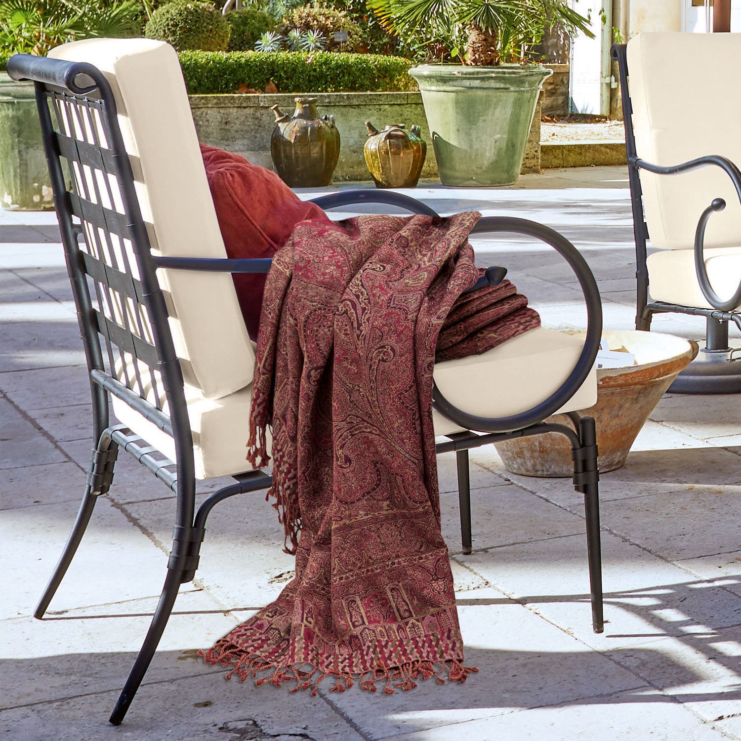 Plaid Nugère Fauteuil en métal noir avec coussin crème et plaid bordeaux à motifs sur terrasse extérieure