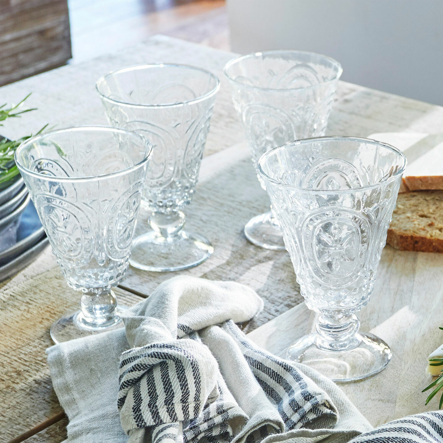 Lot de 4 verres à vin Sarton Ensemble de quatre verres transparents avec motif décoratif sur table en bois avec tissu et pain