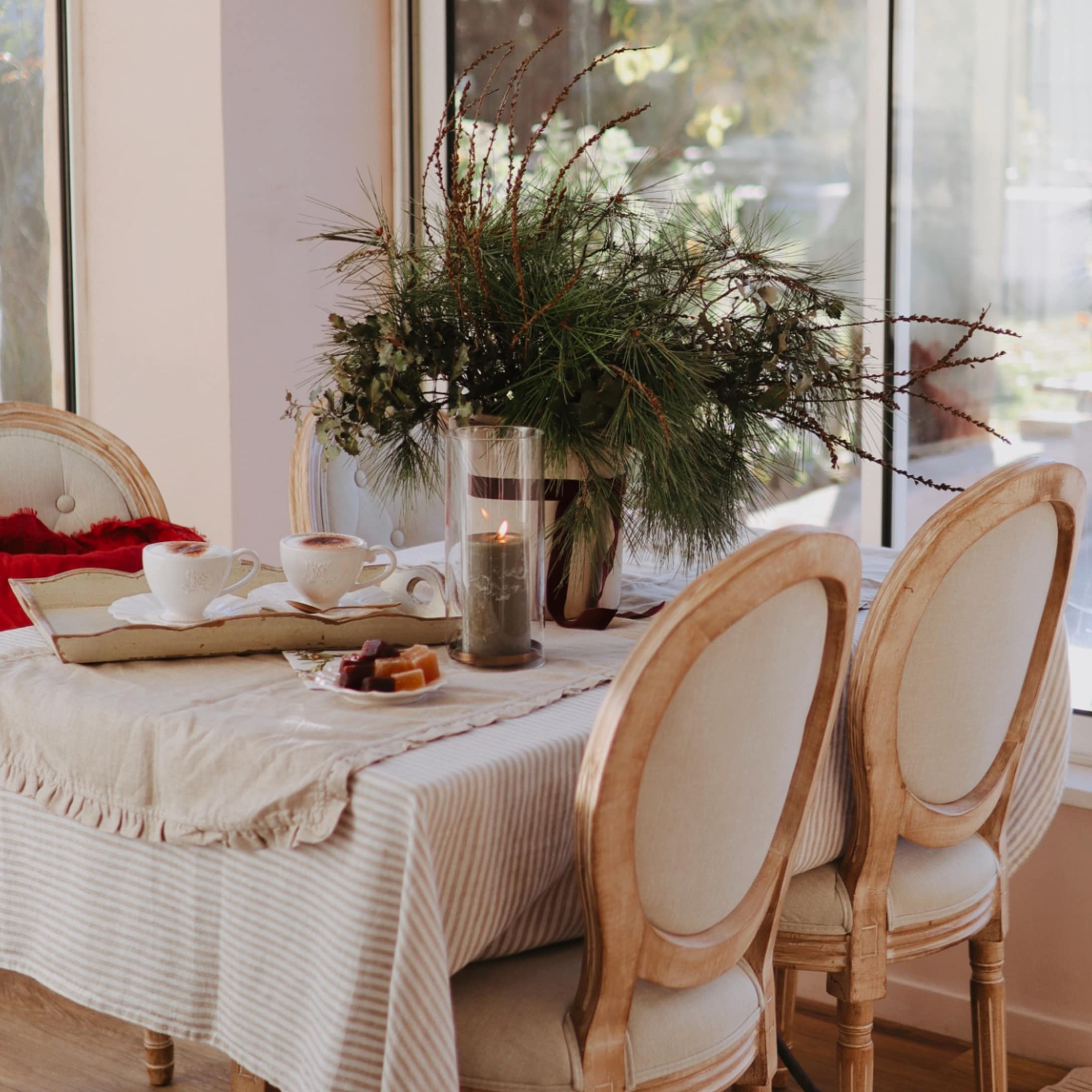 Table chaleureuse avec nappe beige, chaises en bois et décoration de Noël en branches vertes