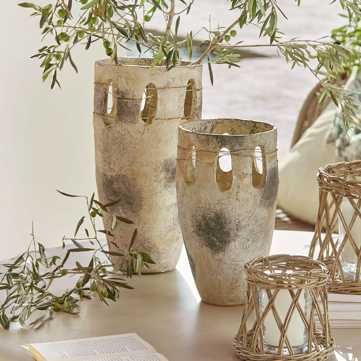Deux vases décoratifs en pierre beige-gris avec des ouvertures et des branches d'olivier sur une table