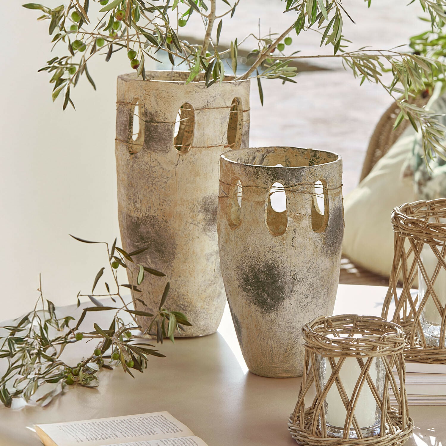 Lot de 2 vases Delunas Deux vases décoratifs en pierre beige-gris avec des ouvertures et des branches d'olivier sur une table