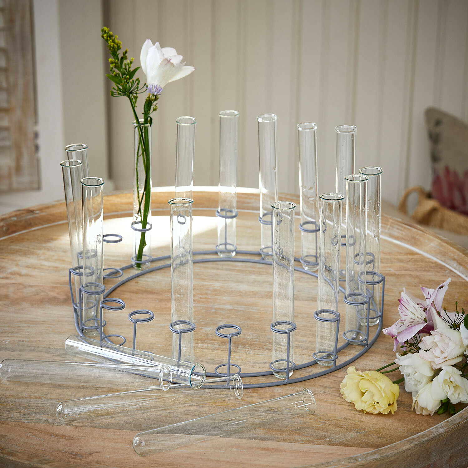 Support rond en métal avec tubes en verre transparents pour fleurs sur une table en bois clair
