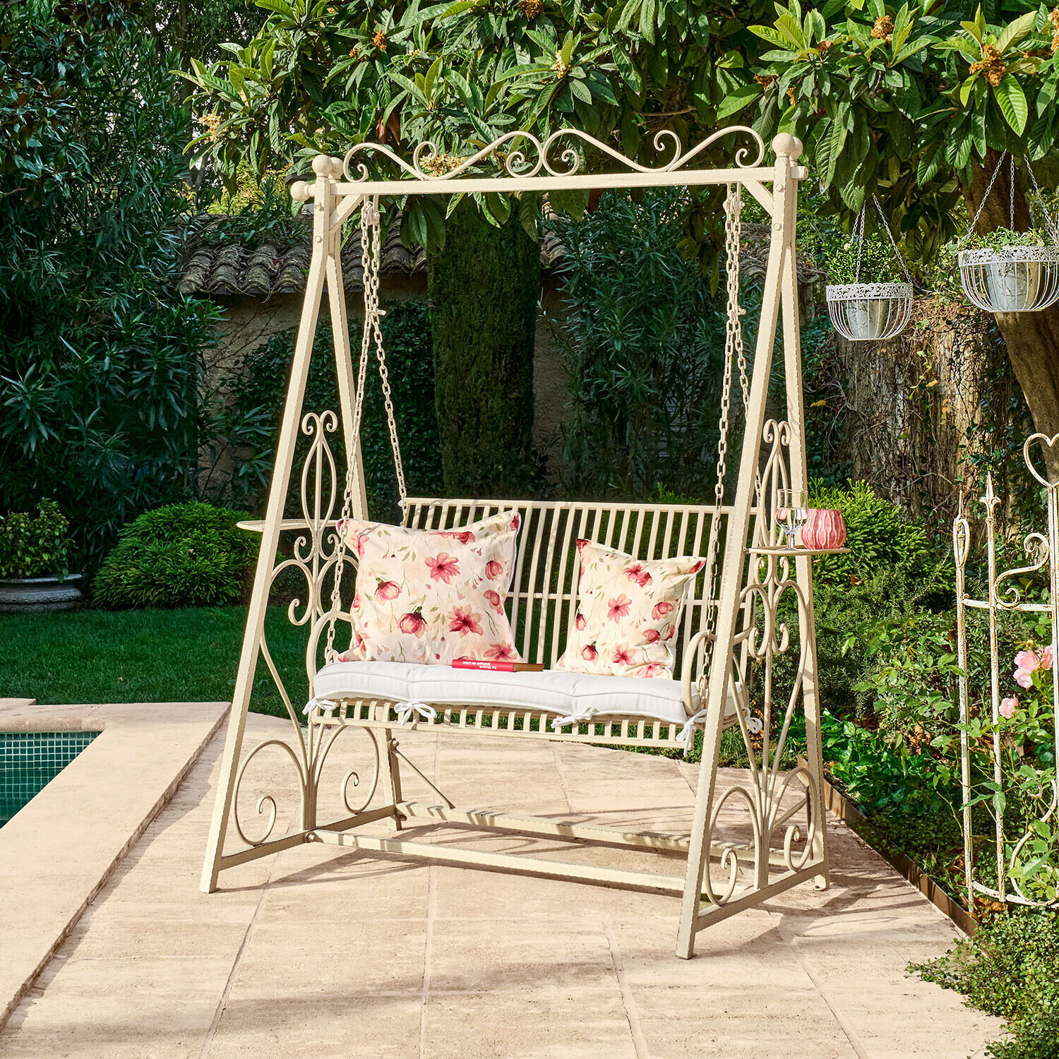 Balançoire de jardin en métal crème avec coussins à motif floral sur terrasse près de la piscine