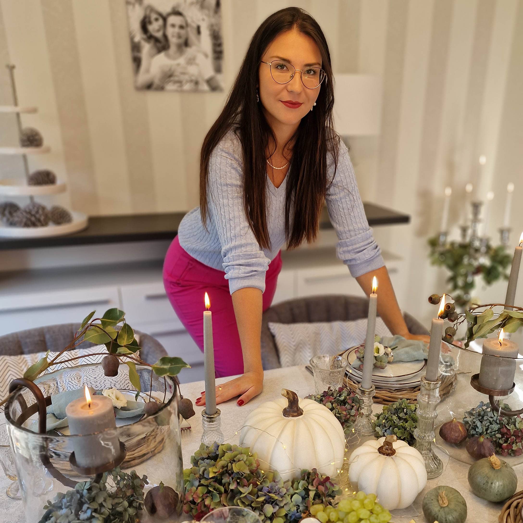 Femme près d'une table décorée avec des citrouilles blanches, bougies et fleurs vertes en intérieur