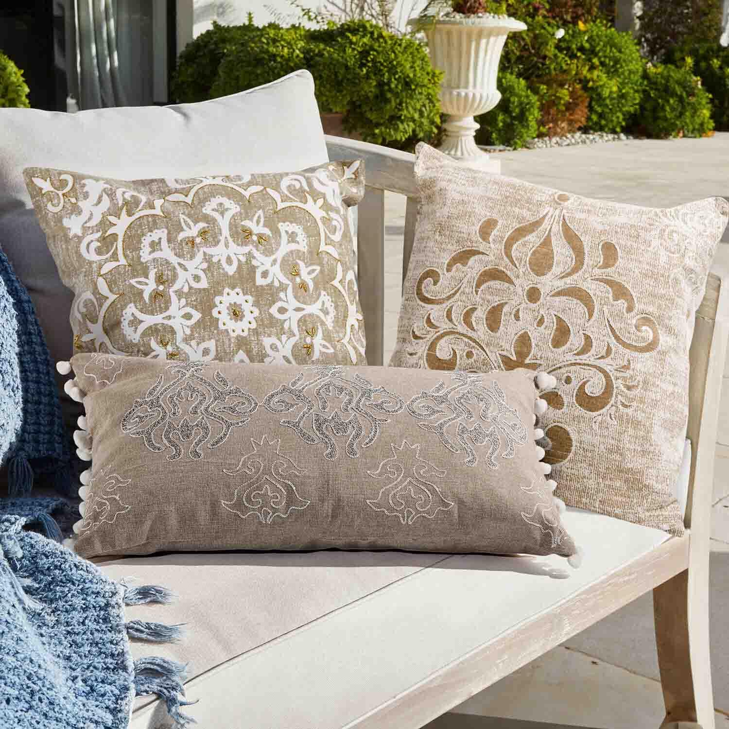 Ensemble de trois coussins décoratifs beige et blanc avec motifs sur un canapé clair en extérieur