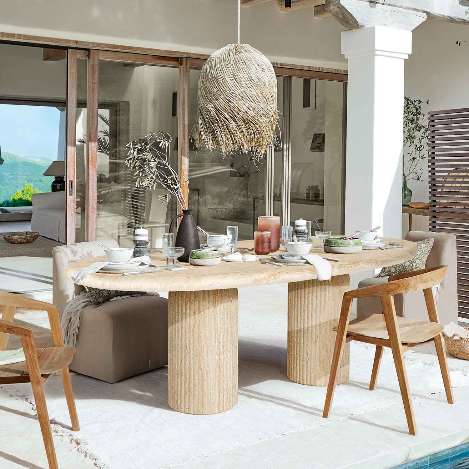 Table à manger en pierre claire avec pieds cylindriques, entourée de chaises en bois et rembourrées dans un espace lumineux