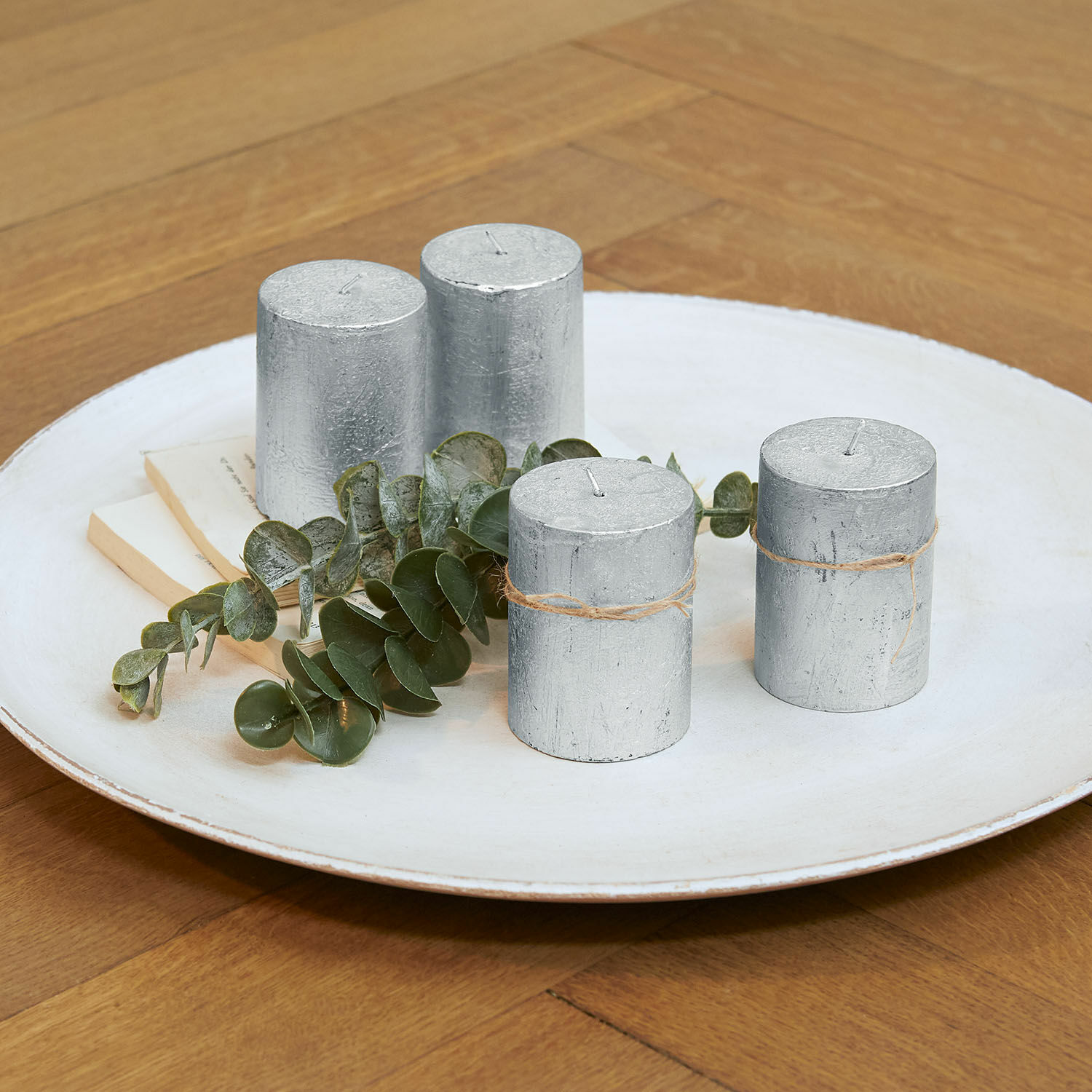 Lot de 4 bougies Virrans Ensemble de quatre bougies cylindriques argentées avec ficelle de jute sur une assiette blanche avec feuilles vertes