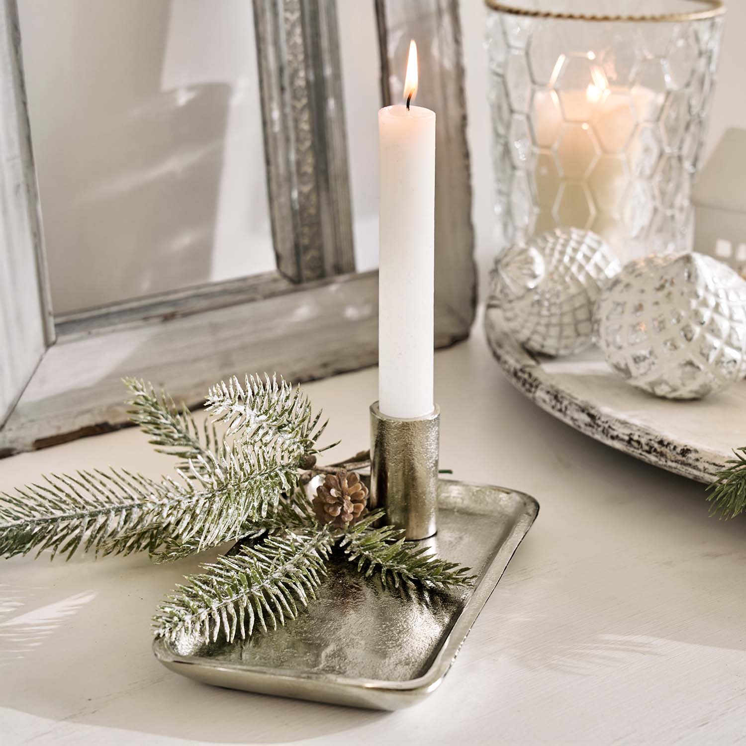 Bougeoir en métal argenté avec une bougie blanche et décoration de branches de sapin sur une table claire