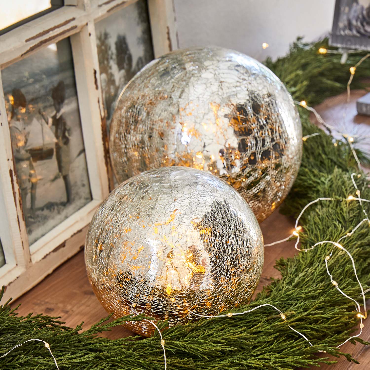 Deux boules décoratives en verre craquelé avec lumière chaude entourées de branches vertes