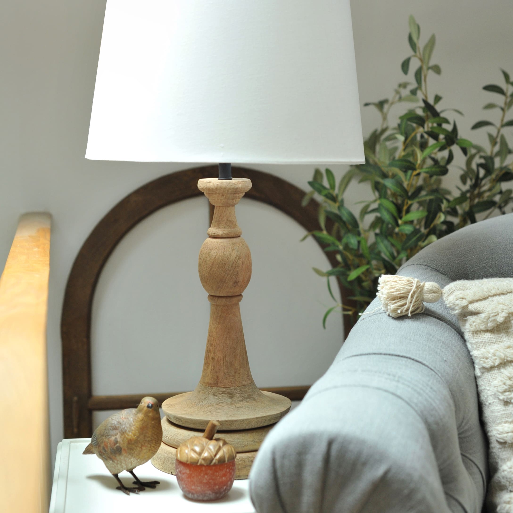 Lampe de table avec base en bois et abat-jour blanc sur une table près d’un canapé gris et décorations