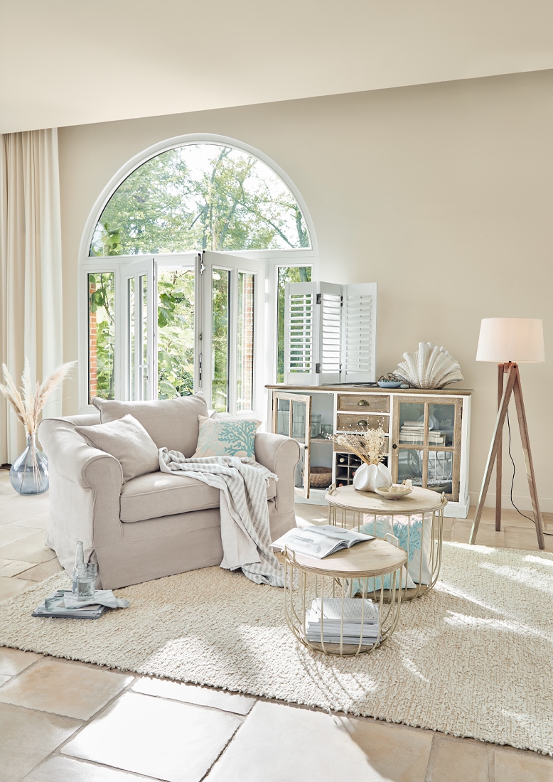 Fauteuil beige confortable avec coussin et plaid dans un salon lumineux avec fenêtre et lampe sur pied