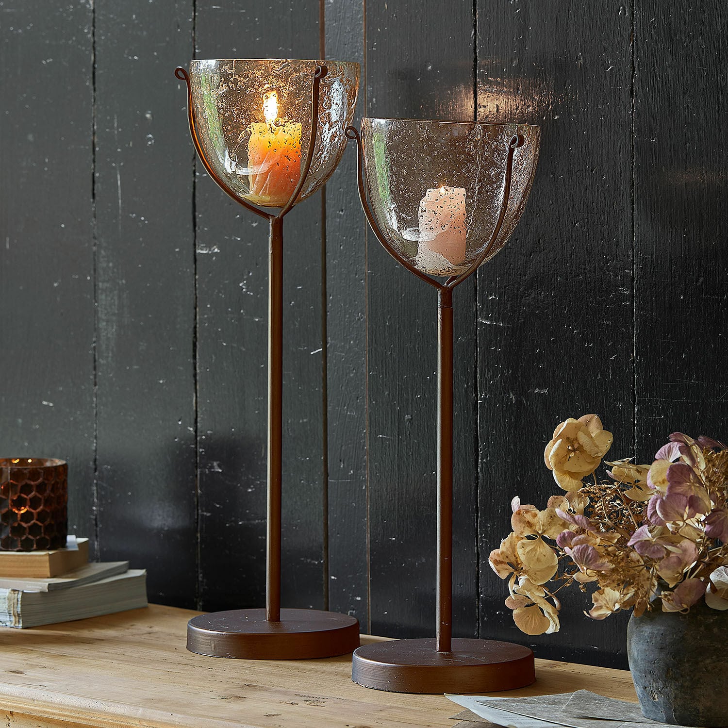Lot de 2 bougeoirs Piacello Deux bougeoirs en métal brun avec verre texturé à bulles et bougies allumées sur table en bois