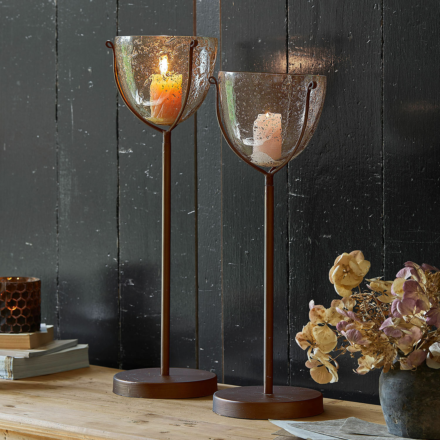 Lot de 2 bougeoirs Piacello Deux bougeoirs en métal brun avec verre texturé à bulles et bougies allumées sur table en bois