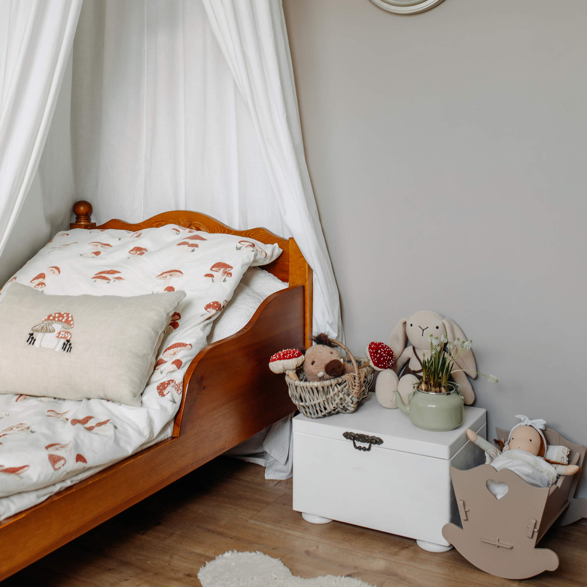 Lit en bois pour enfant avec literie blanche à motifs champignons et peluches sur coffre blanc