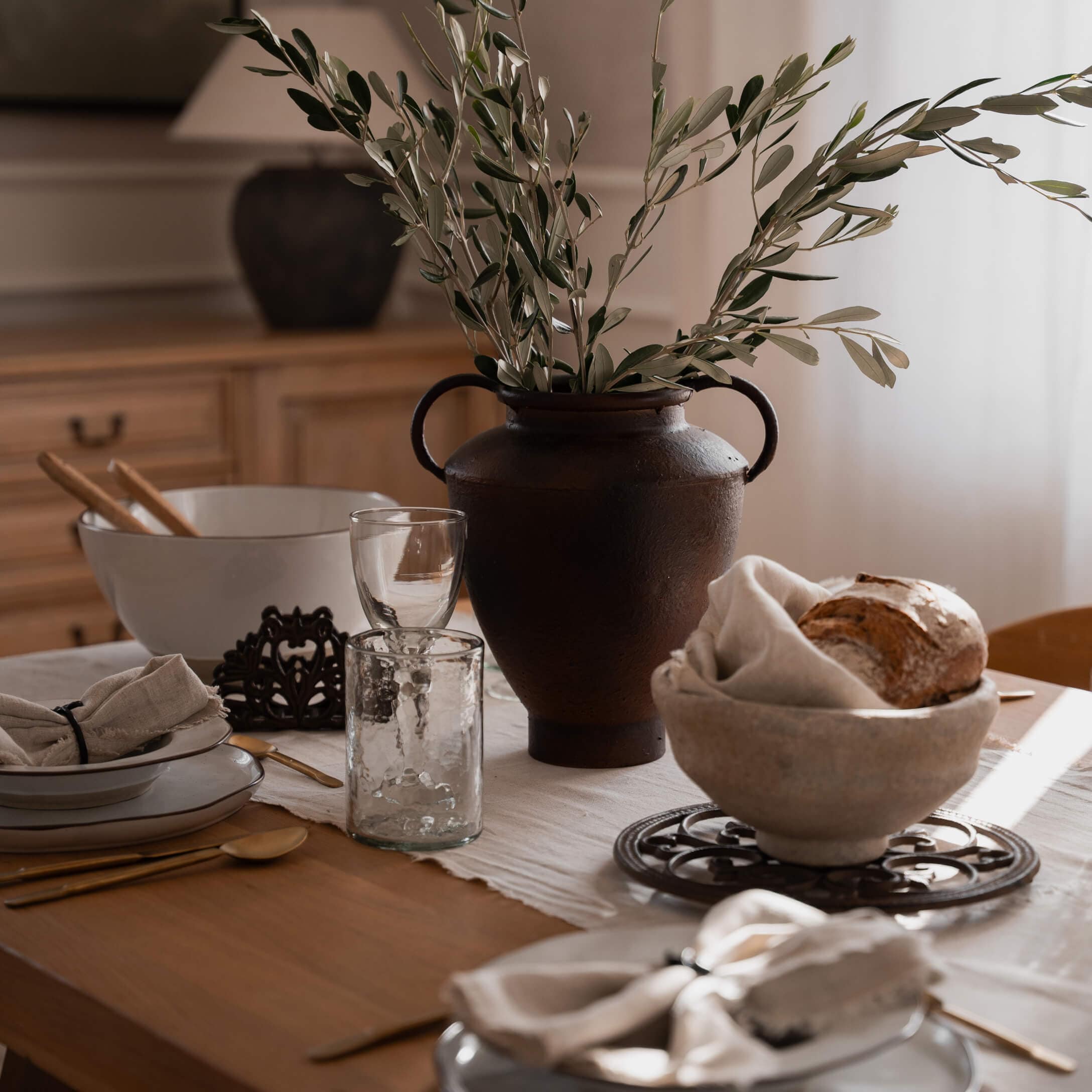 Vase en céramique marron rustique avec branches vertes sur table en bois avec vaisselle