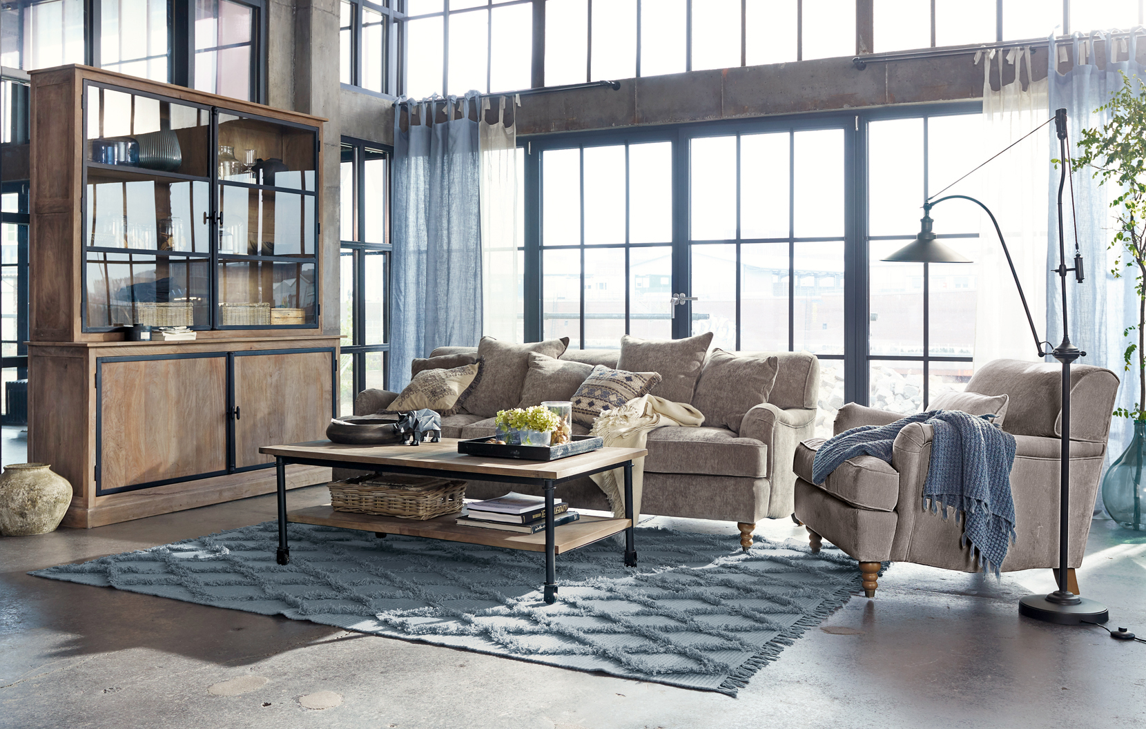 Salon loft chaleureux avec canapé beige, meuble en bois et tapis bleu sur sol en béton