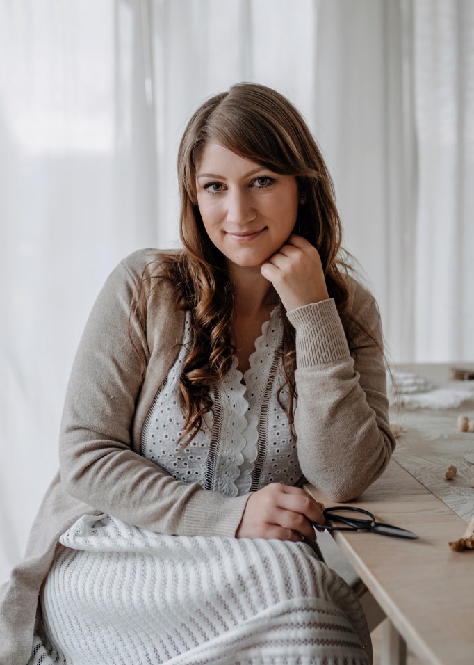 Femme en cardigan beige et robe blanche en dentelle assise à une table en bois avec des ciseaux