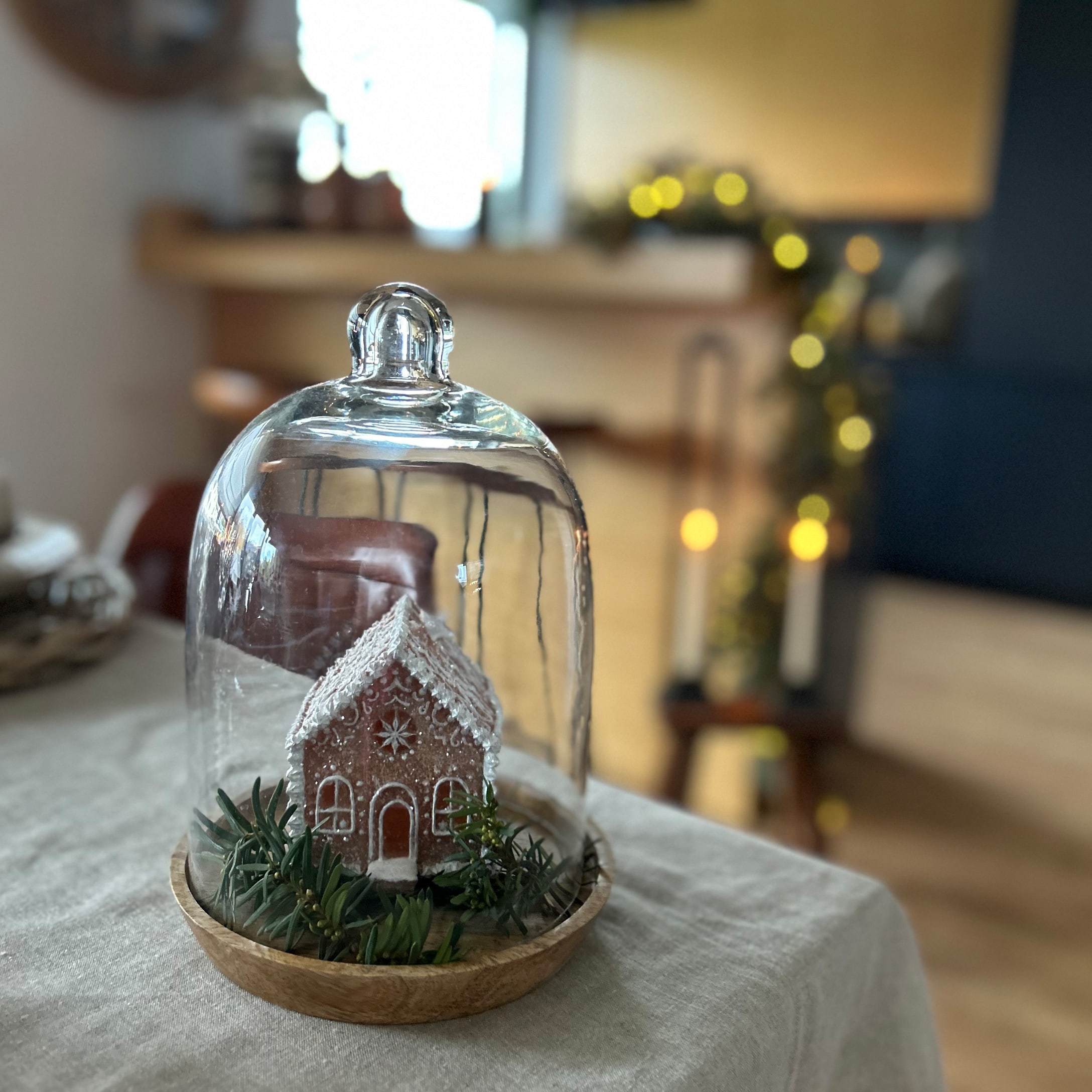 Maison en pain d'épices décorative sous cloche en verre sur socle en bois avec branches vertes