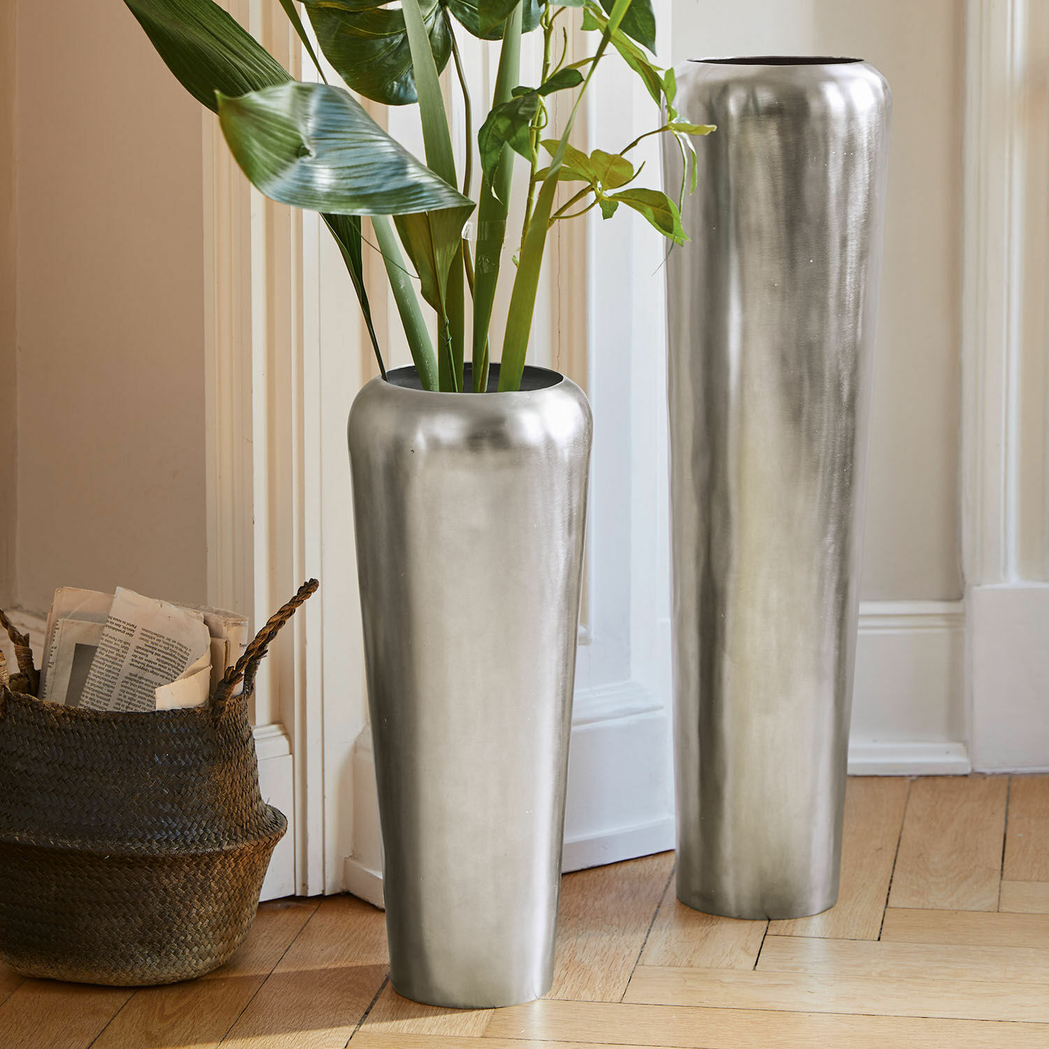 Lot de 2 grands vases Carolan Deux grands vases métalliques argentés posés au sol dans un intérieur lumineux avec plantes vertes