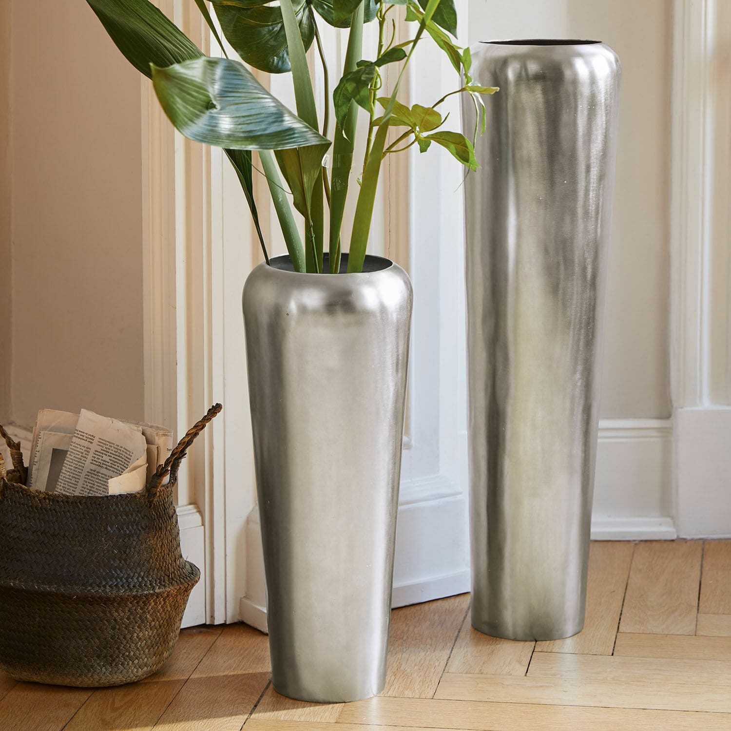 Lot de 2 grands vases Carolan Deux grands vases métalliques argentés posés au sol dans un intérieur lumineux avec plantes vertes