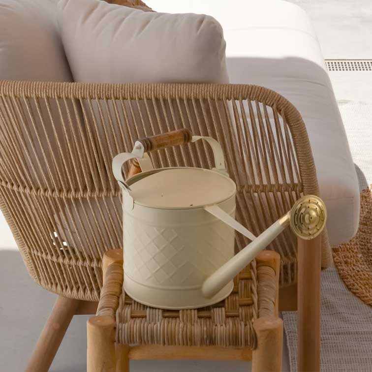Arrosoir en métal crème avec poignée en bois posé sur une chaise en osier, décoration extérieure