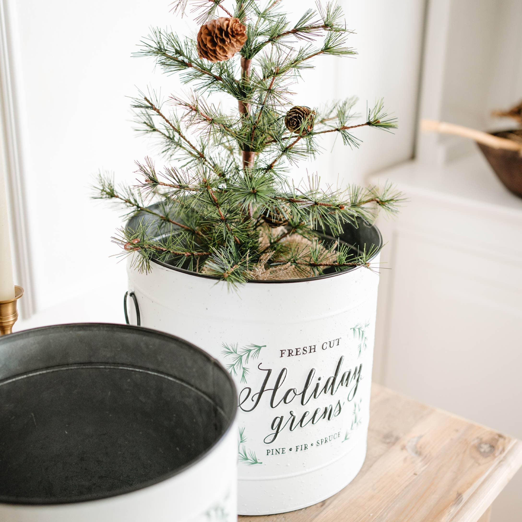 Pot en métal blanc avec branches de pin vertes et pommes de pin sur une table en bois