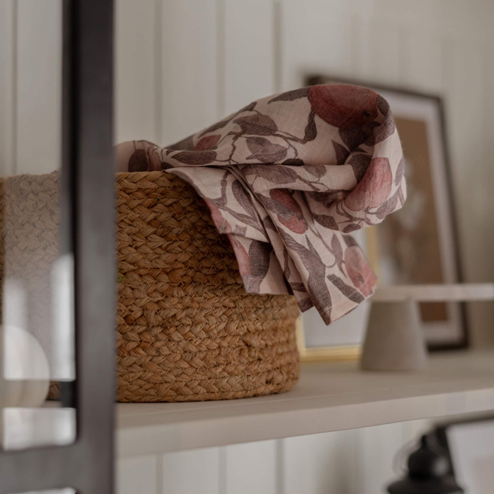 Panier en matériau tressé naturel avec tissu en lin à motif floral rose et brun sur étagère blanche