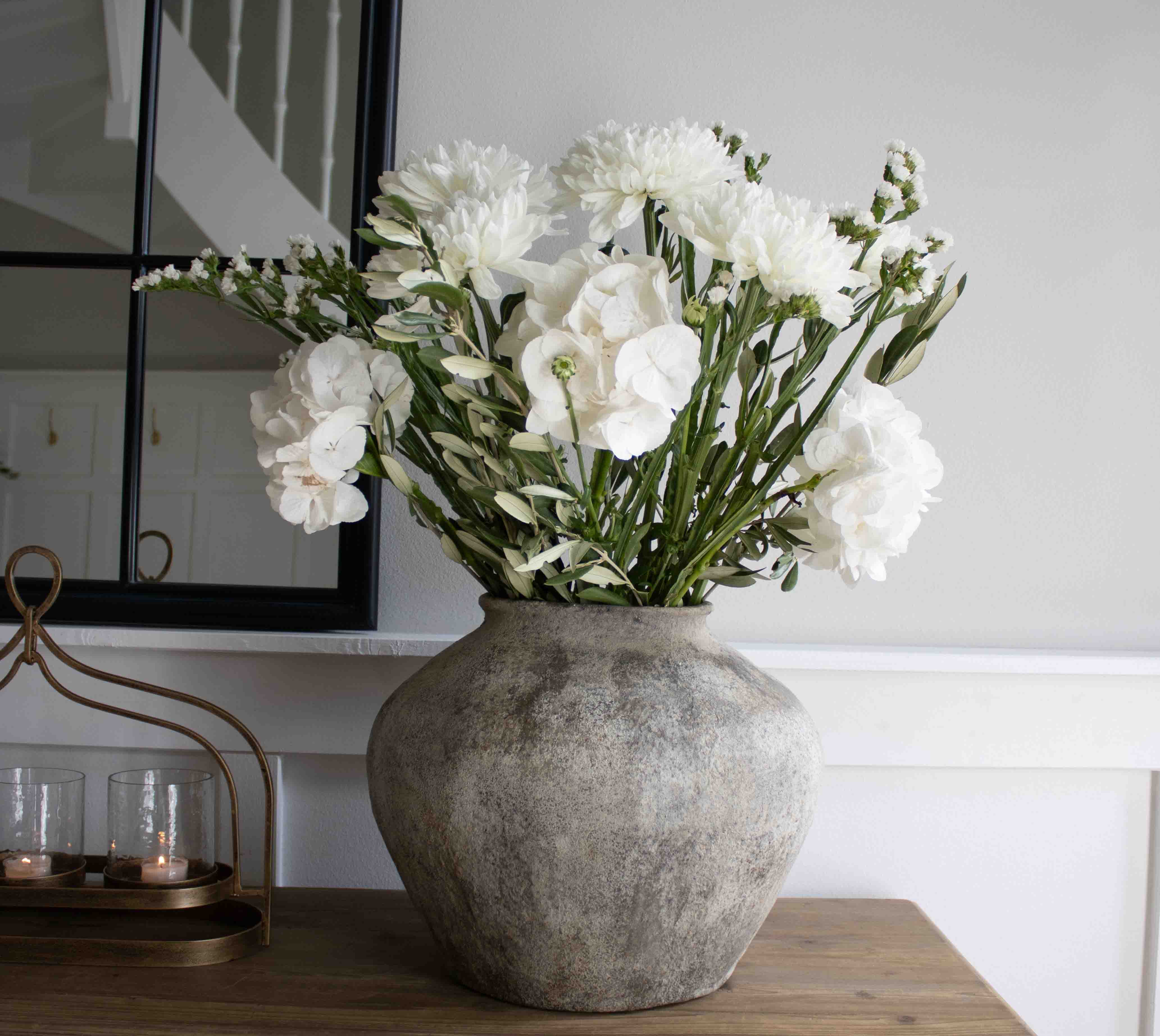Grand vase en pierre grise avec fleurs blanches décoratives sur une table en bois dans un salon