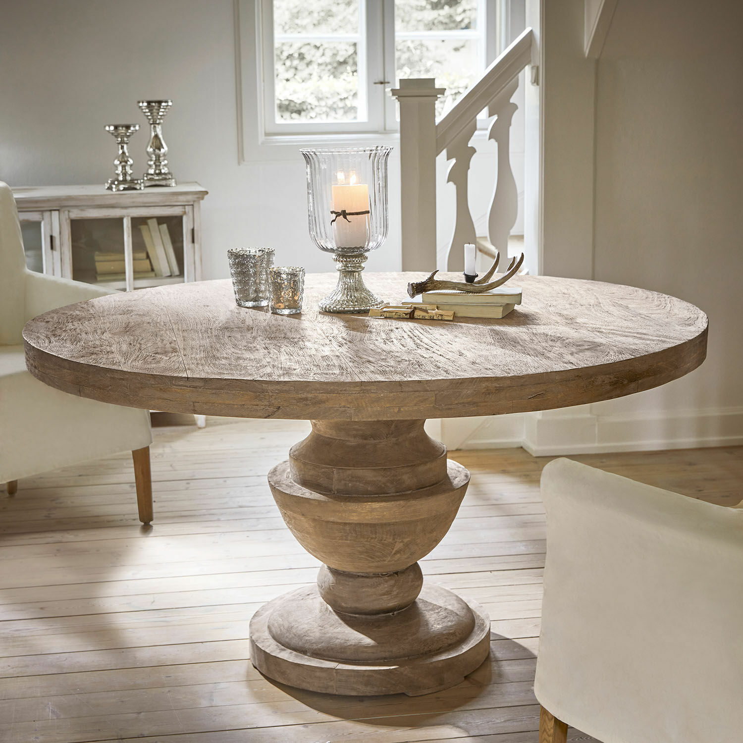 Table ronde en bois de manguier naturel avec bougeoirs décoratifs et livres posés dessus dans une pièce lumineuse
