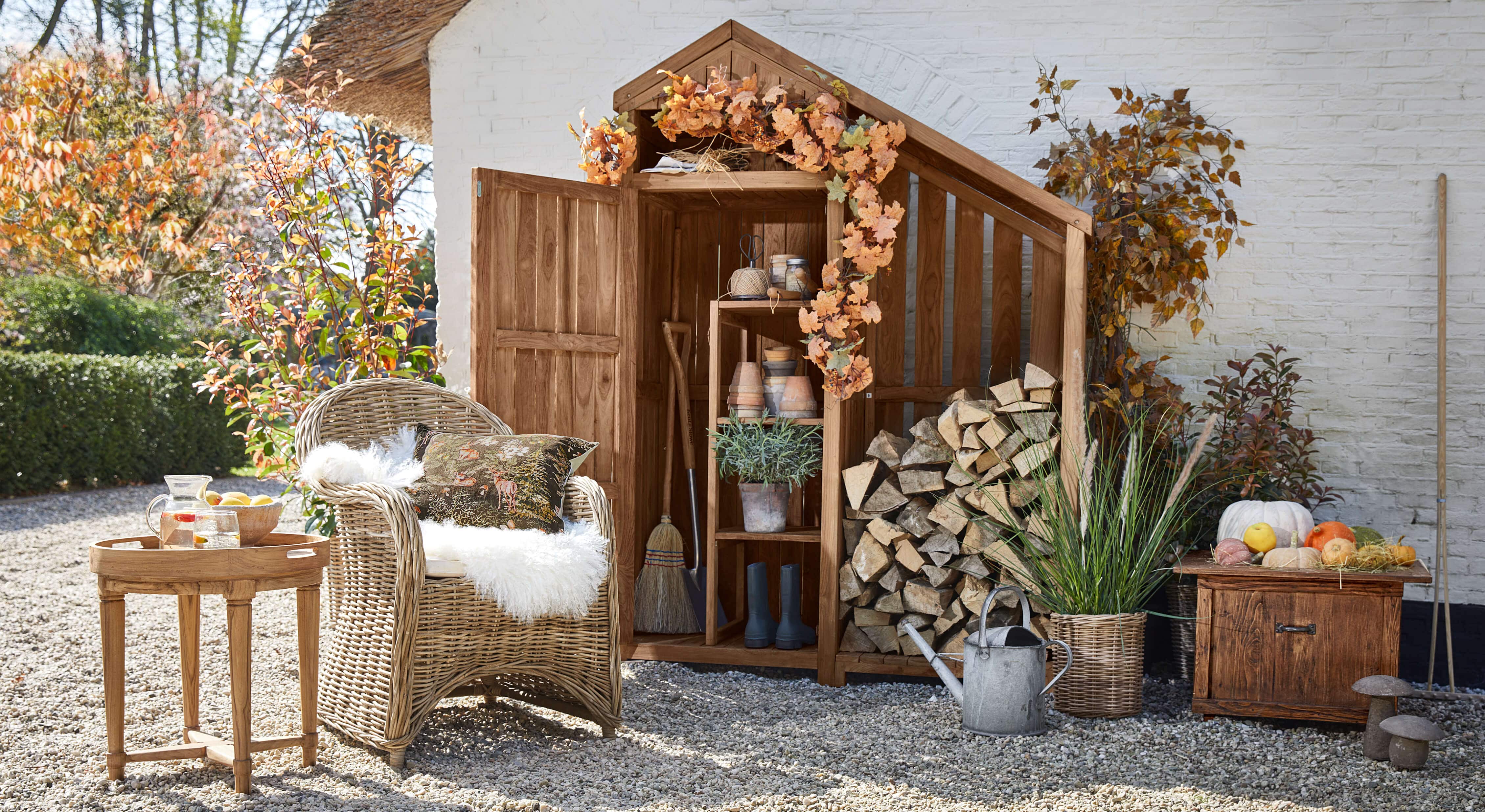 Abri de jardin en bois avec décoration d'automne, fauteuil en osier et table avec carafe sur sol en gravier