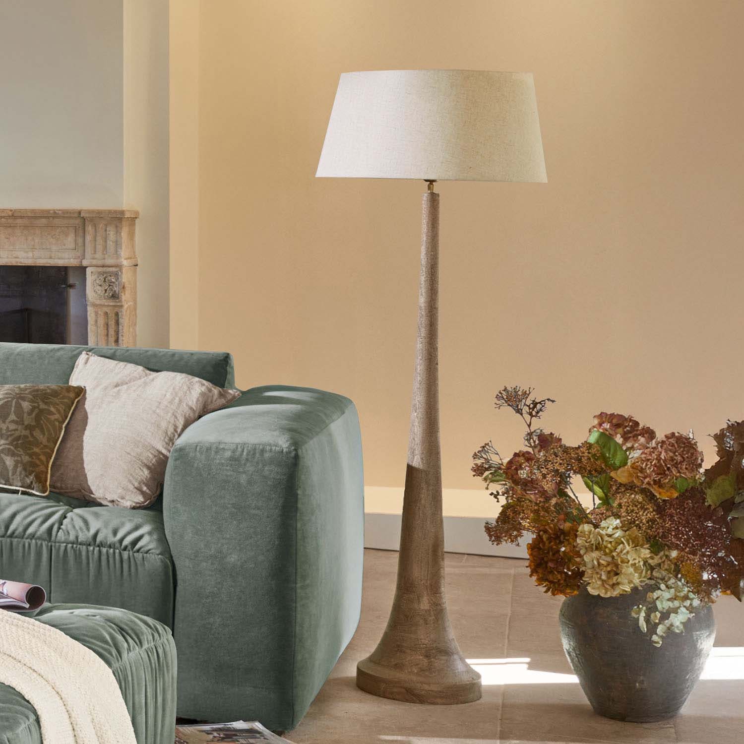 Lampadaire en bois avec abat-jour beige dans un salon moderne avec canapé vert et décor floral