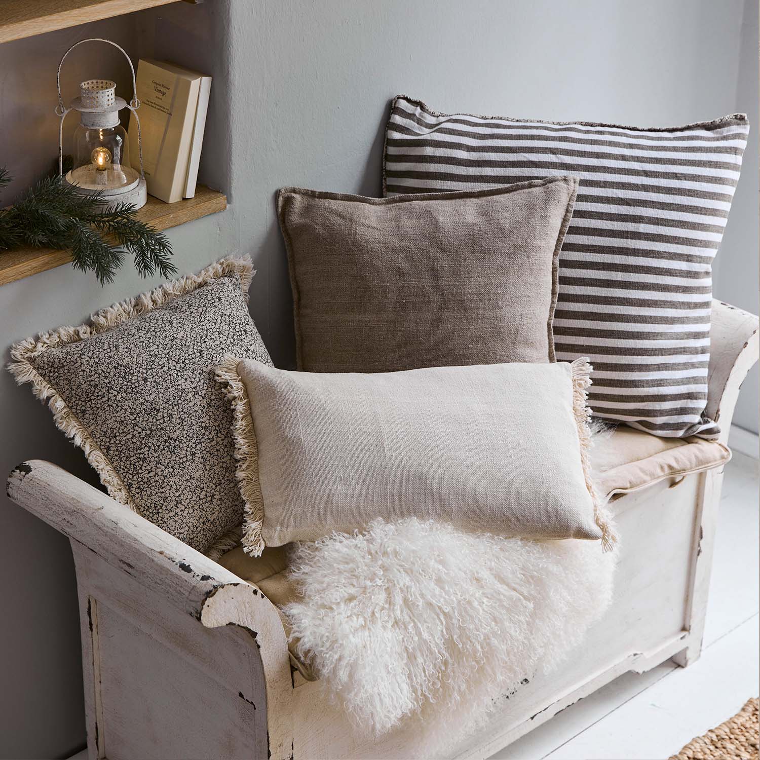 Ensemble de coussins décoratifs beige et marron sur un banc en bois blanc avec couverture en fausse fourrure