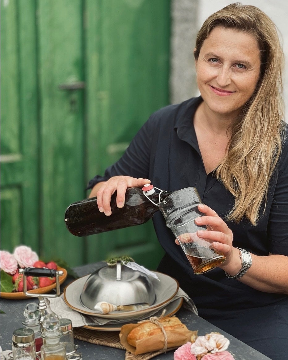 Femme versant une boisson d'une bouteille en verre dans un verre à table avec nourriture et fleurs