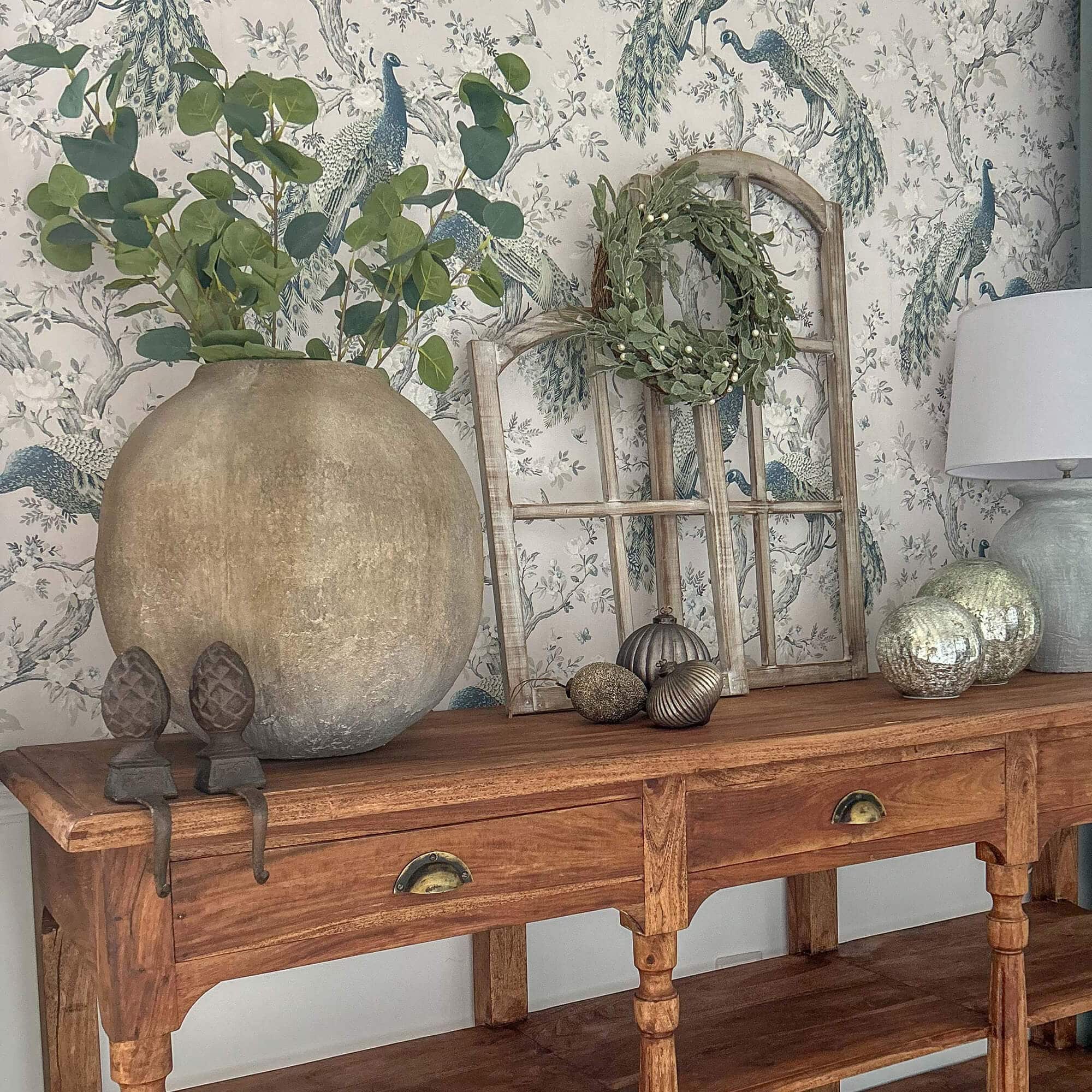 Table en bois avec vase en terre cuite, feuillage vert, lampe et décorations sur le dessus