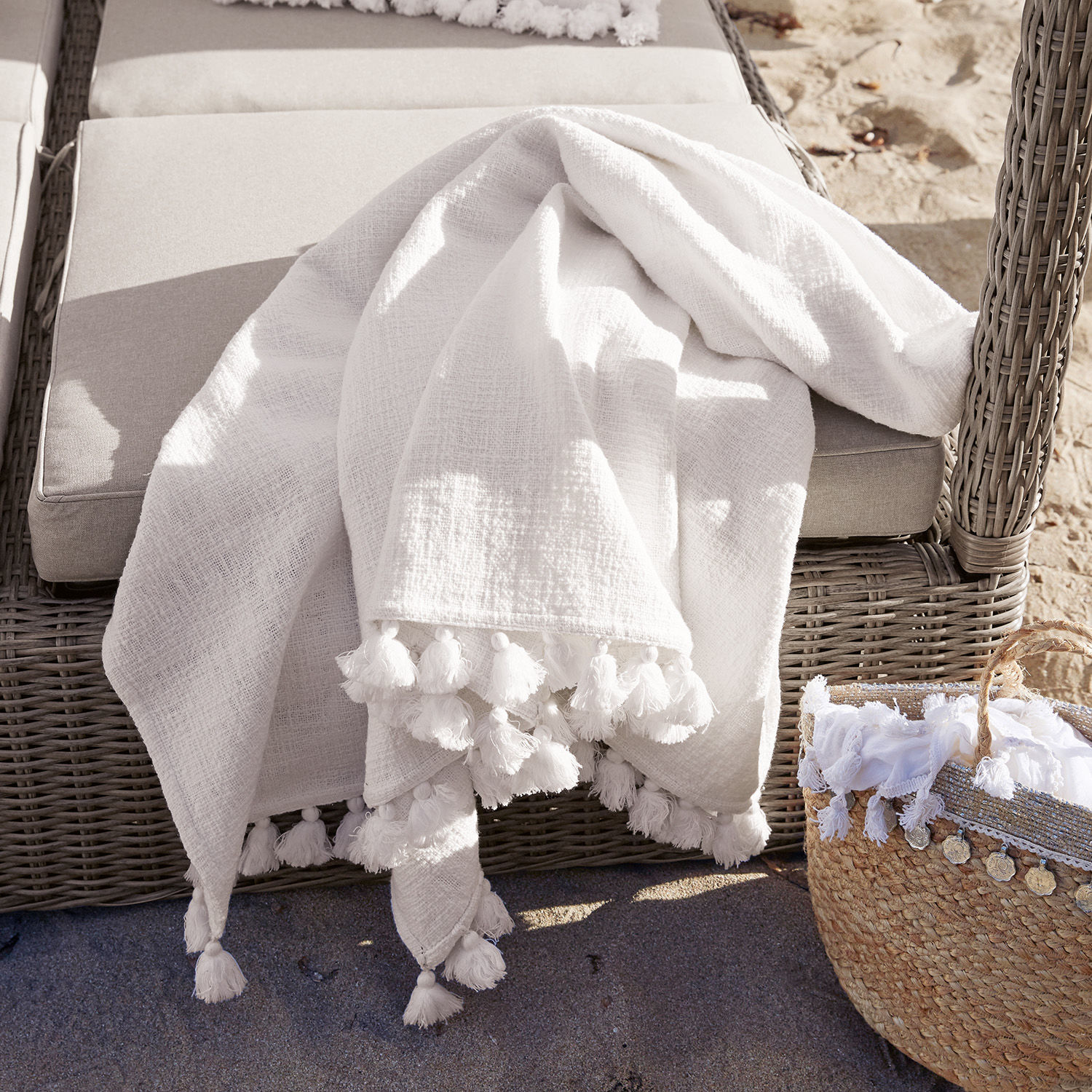 Plaid Amlamé Plaid blanc en coton avec pompons sur fauteuil en osier gris, décoration extérieure de jardin