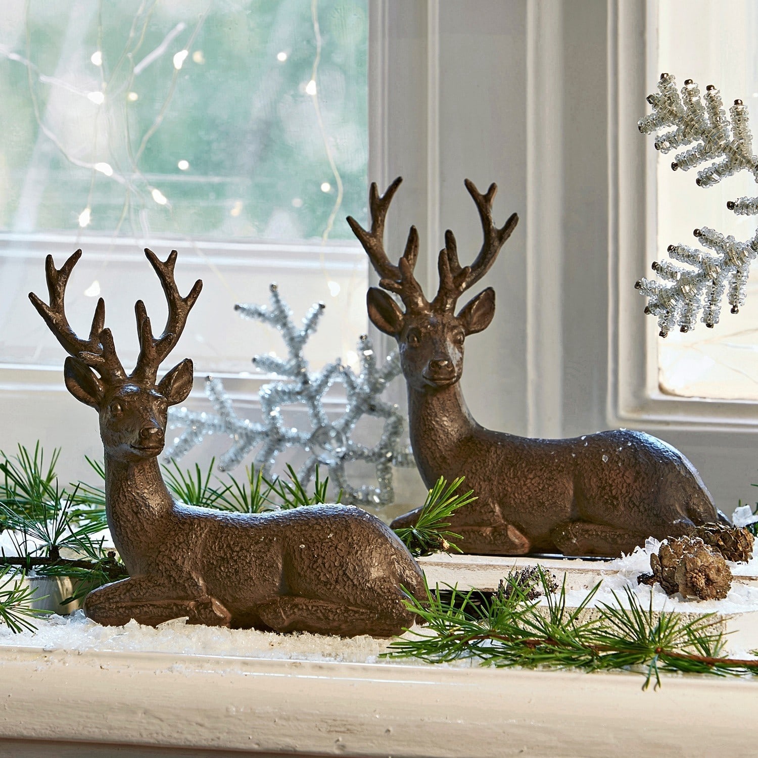 Ensemble de 2 cerfs décoratifs Janville Décorations de rennes en plastique brun sur rebord de fenêtre avec branches vertes et neige artificielle
